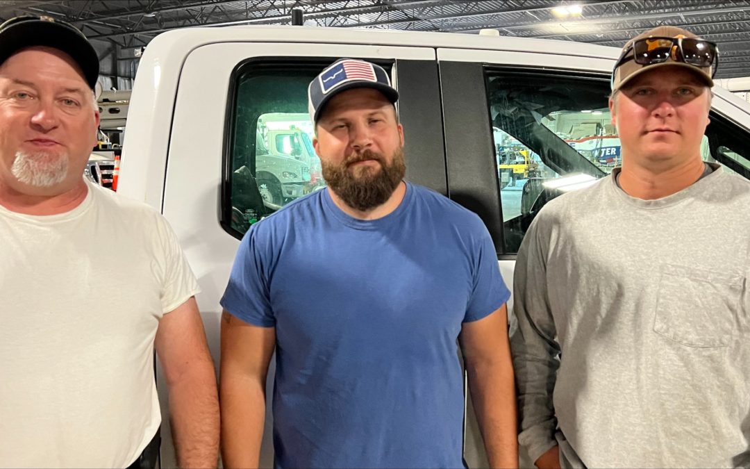 three DTE lineman standing in a row in front of a DTE truck for a photo