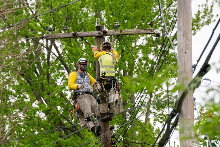 Two men working up high on a utility pole. One man to the left, one in front with his back turned