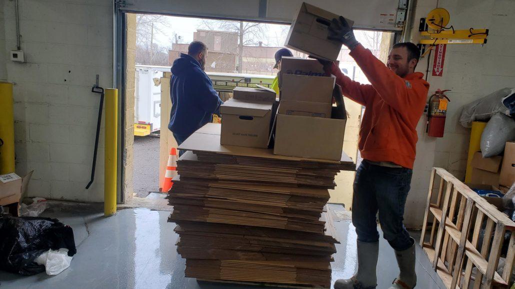 man in orange sweatshirt stacking a box on top of a stack of boxes