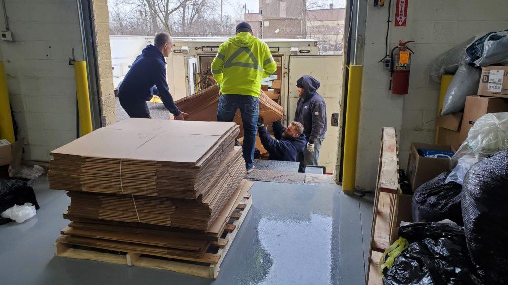 three men loading boxes off of the truck, stack of boxes