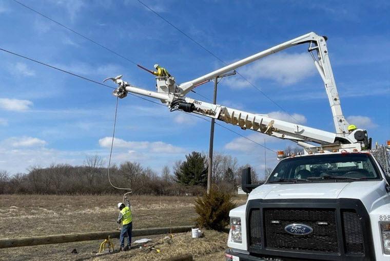 one DTE worker up in a bucket truck working on a power line. Another DTE worker connecting something to a utility pole lying flat