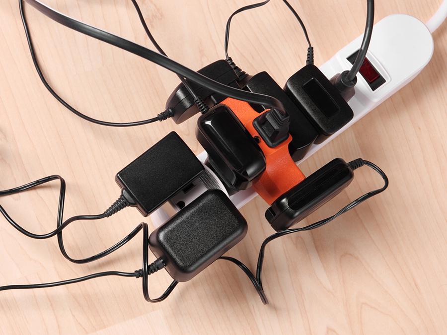Several black cords plugged into every space on a white surge protector that is sitting on a wood floor
