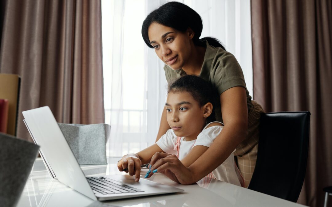 Mother and daughter on a laptop, mother reaching over her shoulder clicking the touchpad